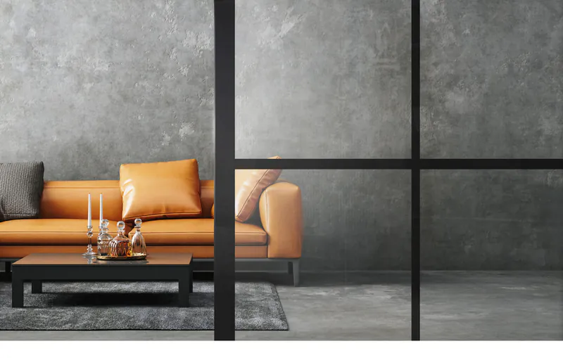 linesplus-in-schwarz-auf-klarglas-scaled-licht-harmonie-holz-disselnmeyer-detail-edbed14b Blick durch eine schwarze Lofttür aus Glas auf ein modernes Wohnzimmer mit orangem Sofa und grauer Betonwand.