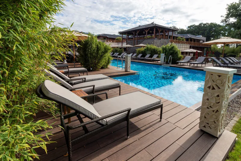 moso-vabali-hamburg-973523a6 Entspannende Atmosphäre im Vabali Spa Hamburg mit bequemen Liegen am Außenpool, umgeben von üppigen Bambuspflanzen.