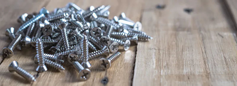 schrauben-02642c26 Ein Haufen silberner Metallschrauben liegt ungeordnet auf einer rustikalen Holzoberfläche.