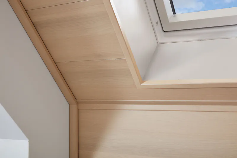Helle Deckenpaneele aus Holz an der Dachschräge rund um ein Dachfenster.