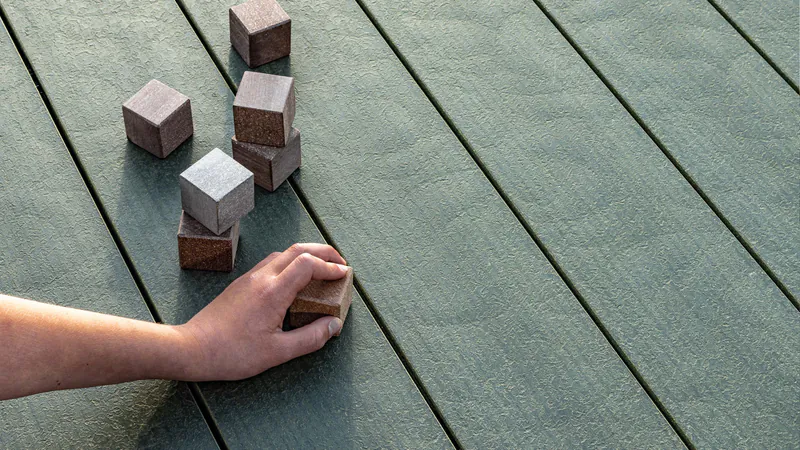 Hand verlegt kleine Holzbausteine als Montagehilfe auf einer Megawood Terrassendiele für eine fachgerechte Verlegung.