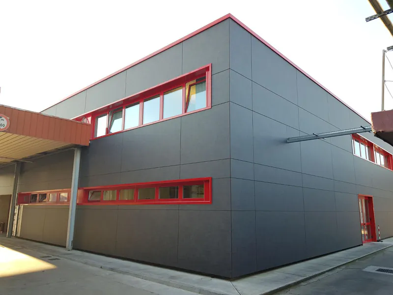 Modernes Industriegebäude mit grauer Trespa Meteon Fassade und roten Fensterrahmen, umgesetzt durch das Unternehmen Disselnmeyer.