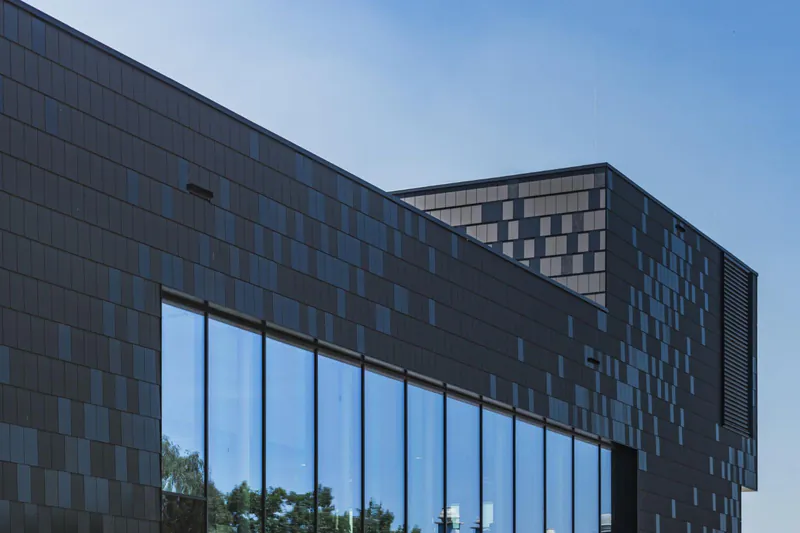 lumen-meteon-trespa-holz-disselnmeyer-1-d4e7b190 Moderne Gebäudefassade aus Trespa Meteon Lumen Fassadenplatten in dunkler Optik mit großflächiger Glasfront und Lichtreflexionen.