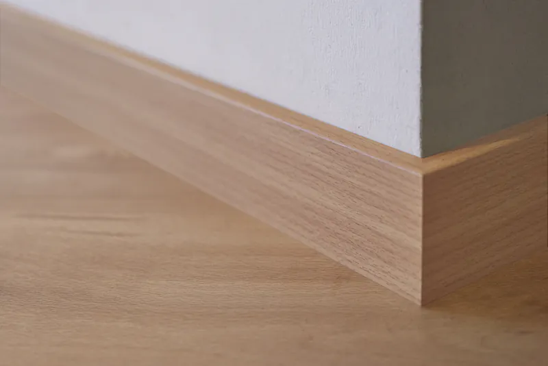 Moderne Fußleiste in heller Holzoptik an einem Wandübergang mit Parkettboden.
