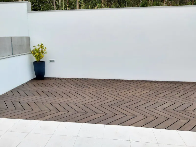 Moderne Terrasse mit Moso Rio Tinto Bambus-Terrassendielen in Fischgrät-Verlegemuster vor einer weißen Wand mit Pflanze.