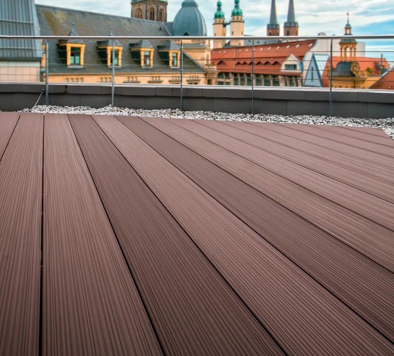 dynum-terrassendiele-megawood-holz-disselnmeyer-62f13222 Hochwertige braune Megawood Terrassendielen auf einer Dachterrasse mit Blick auf eine historische Altstadt.