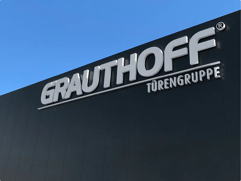 Hochwertiges Firmenschild der GRAUTHOFF Türengruppe in moderner Optik vor blauem Himmel.
