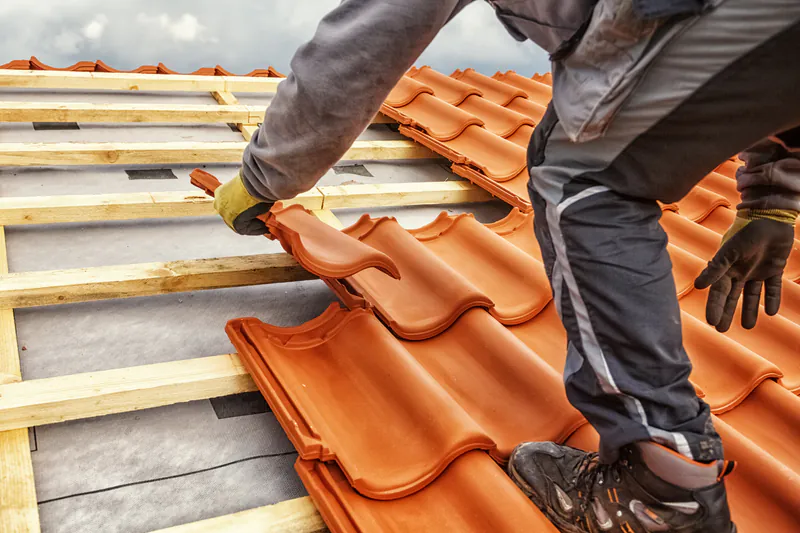Handwerker deckt ein Dach mit roten Dachziegeln auf einer stabilen Unterkonstruktion aus Dachlatten.