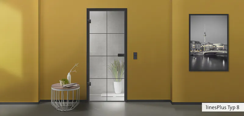Moderne Glastür mit schwarzem Metallrahmen im Industrial-Stil vor einer senfgelben Wand in einem elegant eingerichteten Wohnbereich.