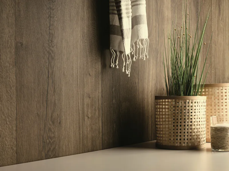 02pi-ap-ph-fur-perfectsense-feelwood-mood-h3149-tm37-01-43b090e3 Wohnliche Wandgestaltung mit hochwertigen PerfectSense Feelwood Paneelen in dunkler Holzoptik, dekoriert mit einer Pflanze im Rattankorb und einem Textiltuch.