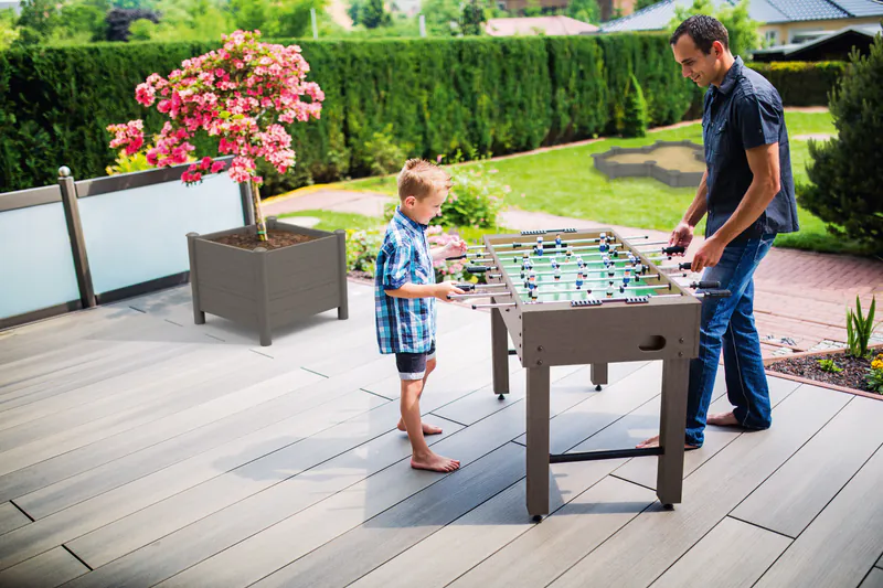 signum-terrassendiele-megawood-holz-disselnmeyer-dcecb709 Vater und Sohn spielen Kicker auf einer modernen Megawood Signum Terrassendiele im heimischen Garten.