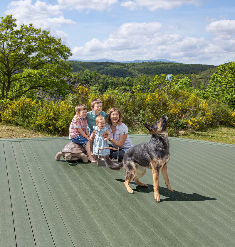 delta-terrassendiele-megawood-holz-disselnmeyer-0050ba42 Familie mit Hund auf einer weitläufigen Terrasse aus grünen Megawood Delta Terrassendielen von Holz Disselnmeyer.