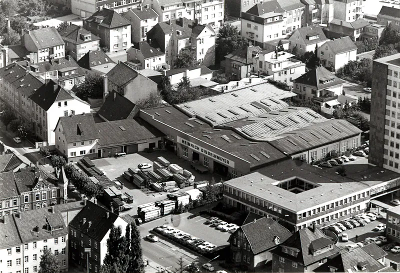 Schwarz-Weiß-Luftaufnahme des Firmengeländes von Holz Disselnmeyer mit Lagerhallen, Bürogebäude und angrenzender Wohnbebauung.